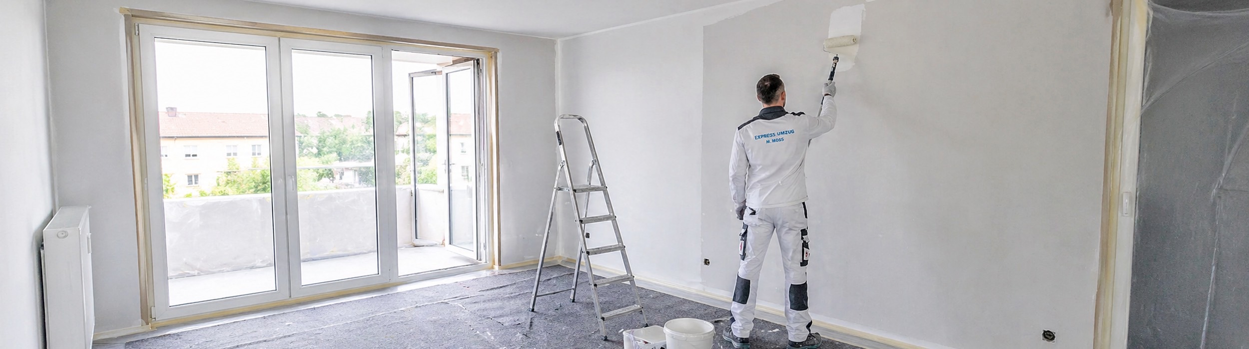 Mitarbeiter von Express Umzug Hildesheim bei Malerarbeiten in einer hellen Wohnung, mit abgeklebten Flächen, Leiter und vorbereitetem Raum für eine saubere Renovierung.