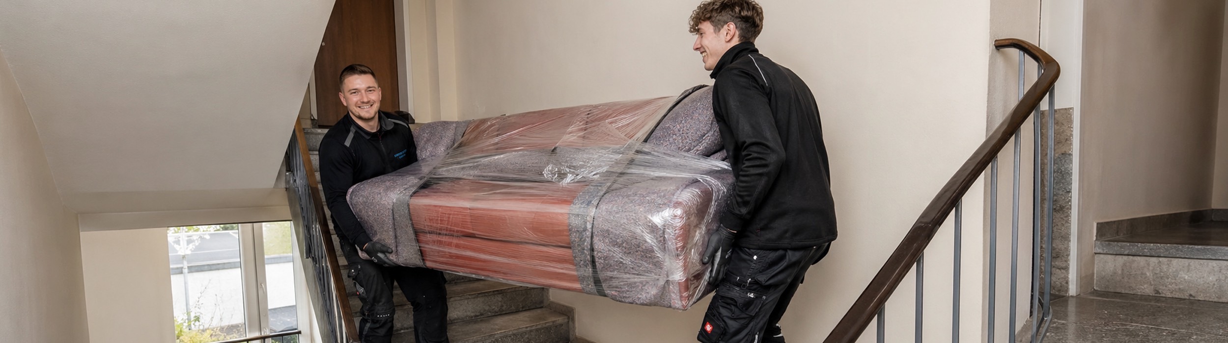 Möbeltransport in Hildesheim mit Express Umzug: Ein Sofa wird sicher verpackt und fachgerecht durch das Treppenhaus getragen.